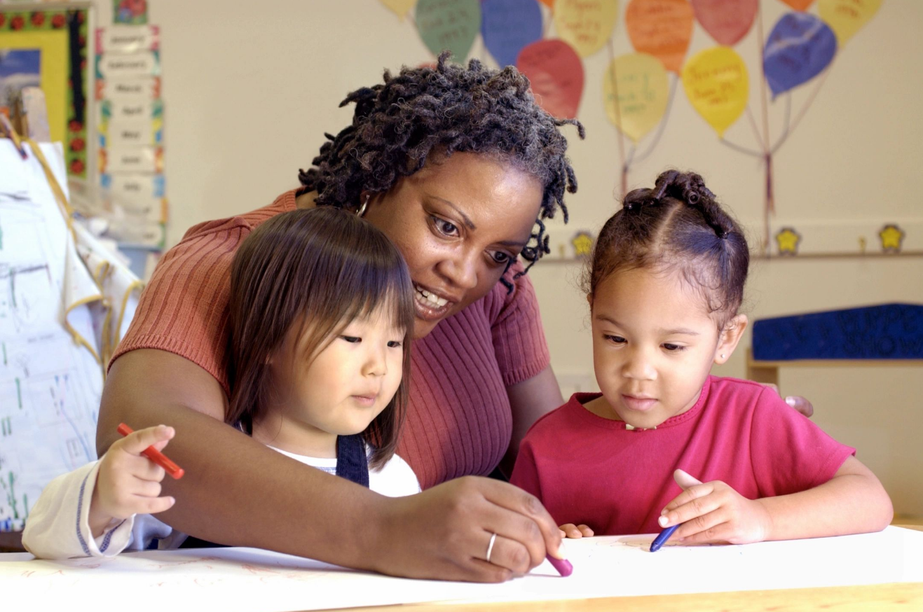 A woman and two young girls drawing on paper.