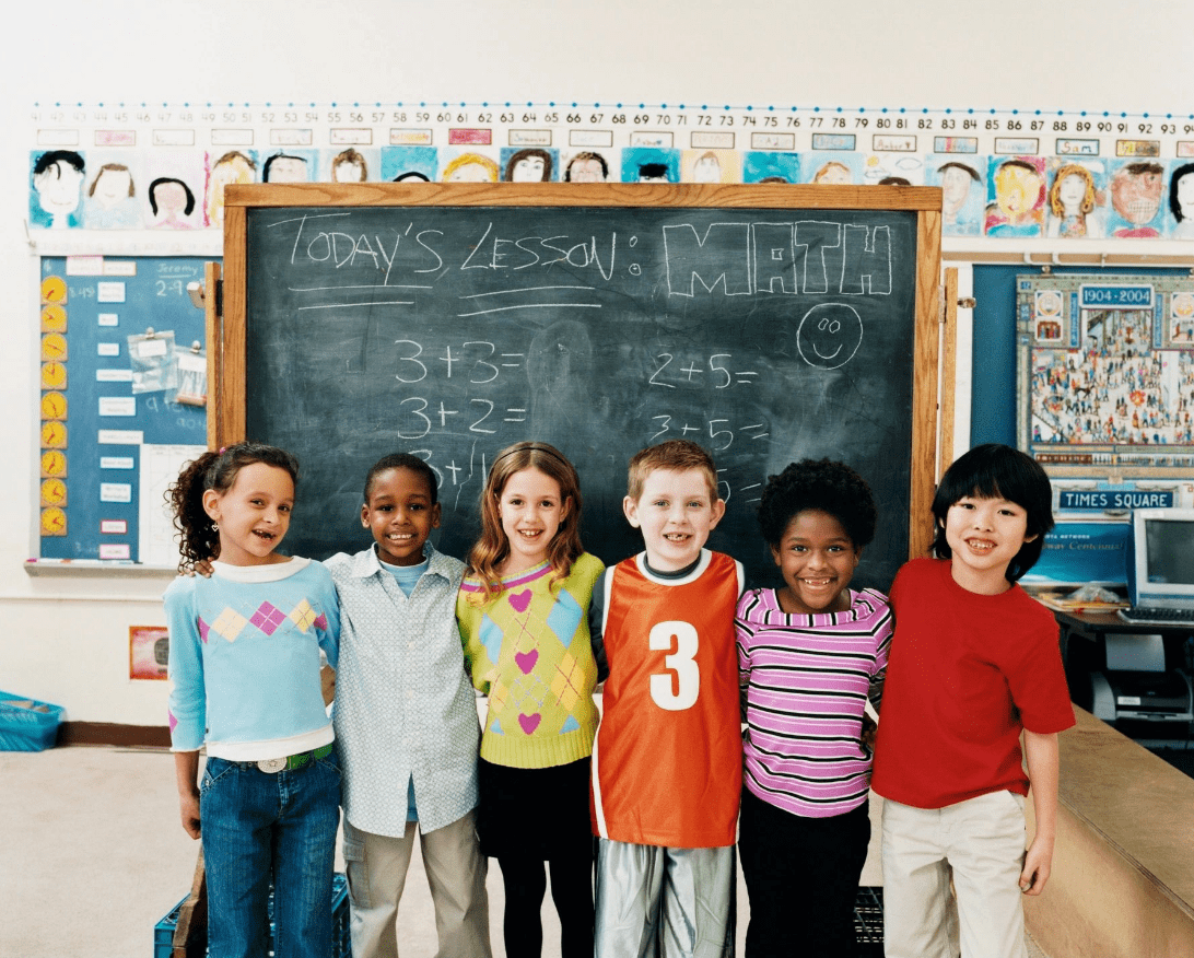 A group of children standing in front of a chalkboard. They are smiling for the camera.
